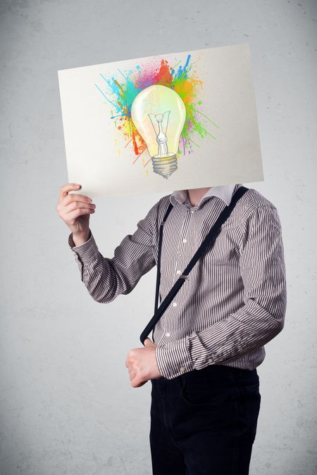 Businessman holding a cardboard with coloured paint splashes and lightbulb in front of his head