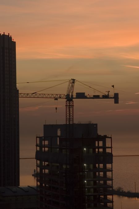 Silhouette of construction crane at dawn, with background of lake and sky