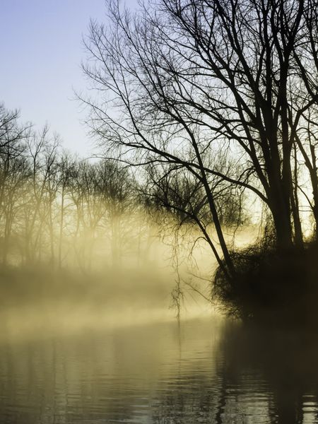 Promise of peaceful illumination: Rays from rising sun light up morning mist over a quiet river early in northern spring
