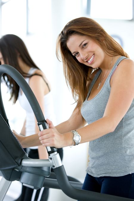 Beautiful gym woman exercising on a cardio machine smiling