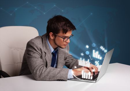 Young man sitting at desk and typing on laptop with diagrams and graphs comming out