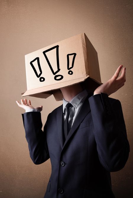 Businessman standing and gesturing with a cardboard box on his head with exclamation point