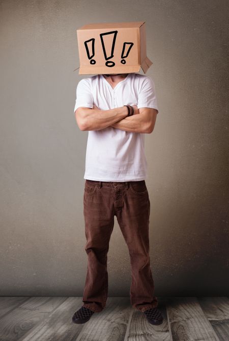 Young man standing and gesturing with a cardboard box on his head with exclamation point