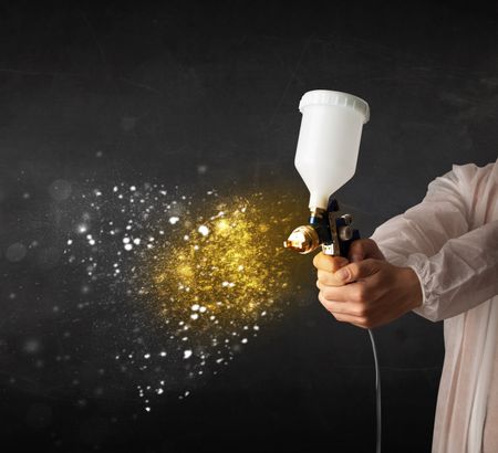 Worker with airbrush painting with glowing golden paint and particles