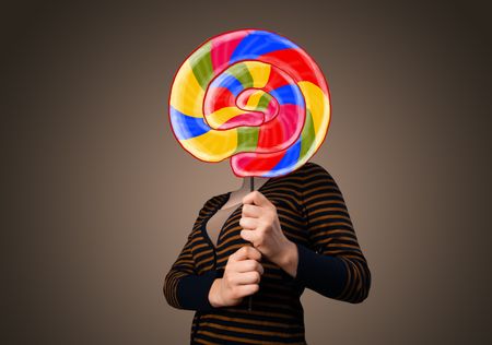 Young lady holding a colorful striped lollipop in front of her head