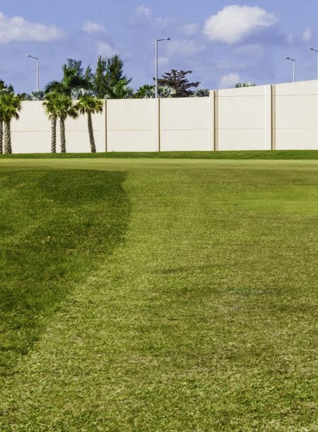 High concrete wall built to stop errant golf balls before they can hit people or vehicles passing by dogleg of golf course in Florida