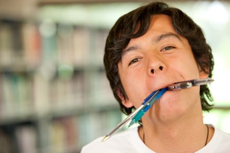 Student in a library with his mouth full of pens and pencils