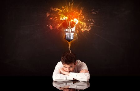 Depressed businessman sitting under a blowing idea bulb