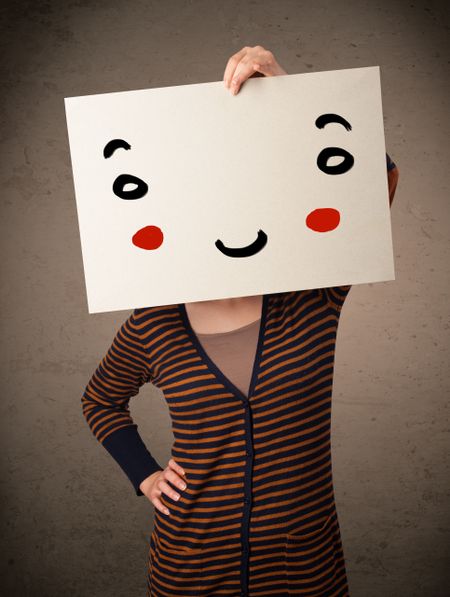 Young woman holding a cardboard with a smiley face on it in front of her head