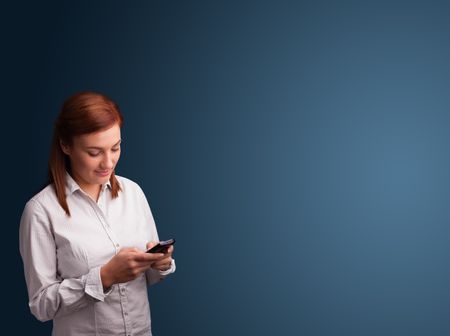 Pretty young woman standing and typing on her phone with copy space