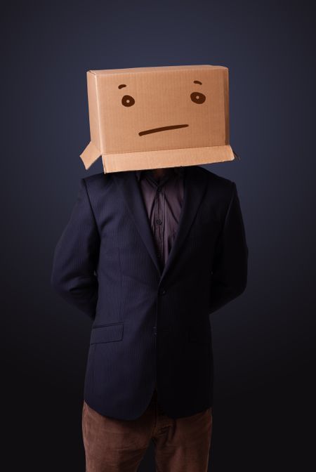 Young man standing and gesturing with a cardboard box on his head with straight face