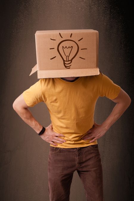 Young man standing and gesturing with a cardboard box on his head with light bulb