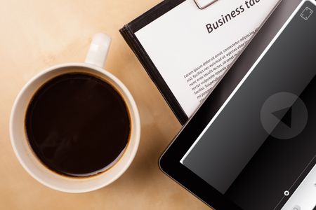 Workplace with tablet pc showing media player and a cup of coffee on a wooden work table close-up