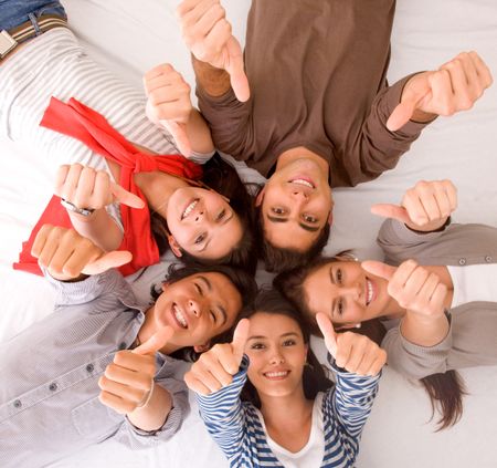 Group of friends with their heads together on the floor with thumbs up - isolated