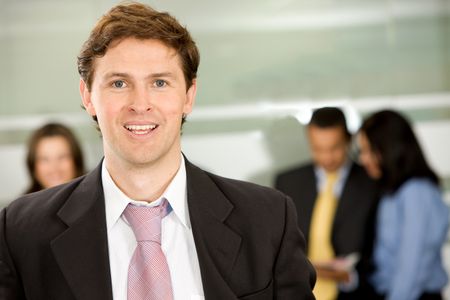 Businessman smiling in an office with his team behind him