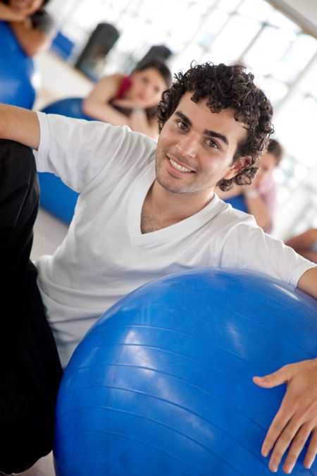 handsome man portrait at the gym smiling and leaning on a pilates ball