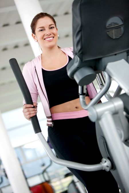Beutiful gym woman exercising on a cardio machine smiling