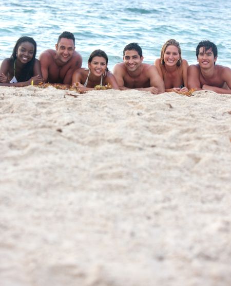 Happy group of friends smiling and lying on the floor at the beach