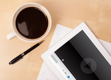 Workplace with tablet pc showing media player and a cup of coffee on a wooden work table close-up