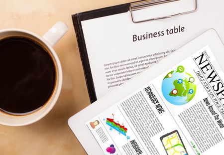 Workplace with tablet pc showing news and a cup of coffee on a wooden work table close-up