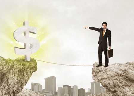 Businessman standing on the edge of mountain with a shining dollar mark on the other side 