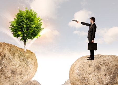 Businessman standing on the edge of rock mountain with a tree on the other side 