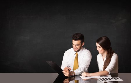 Business couple sitting at black table on black background