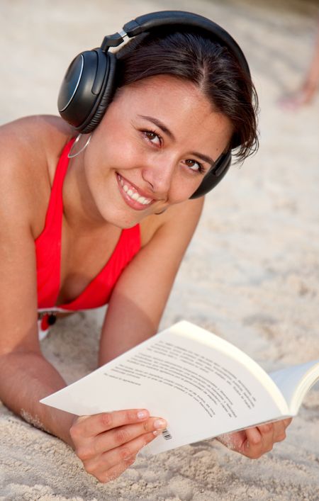 Woman reading a book and listening music on the beach
