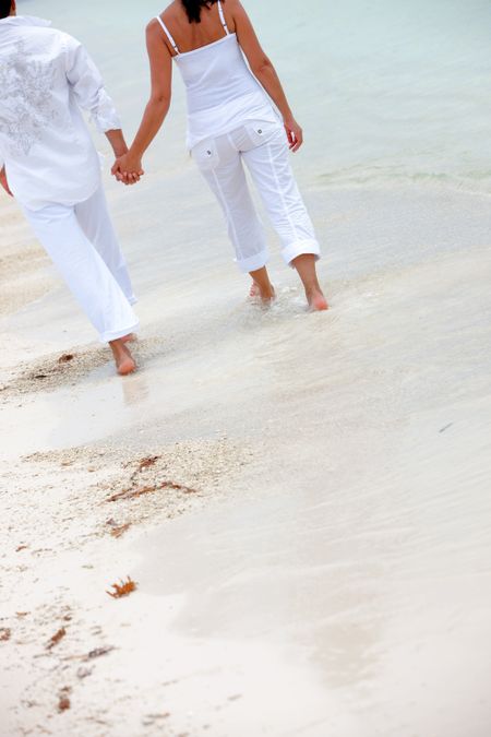 rear view of a couple holding hands and walking on the beach