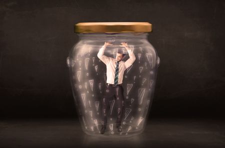 Business man trapped in jar with exclamation marks concept on bakcground