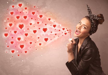 Pretty young girl blowing valentine red heart symbols 