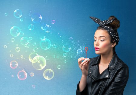Pretty lady blowing big colorful bubbles on blue background