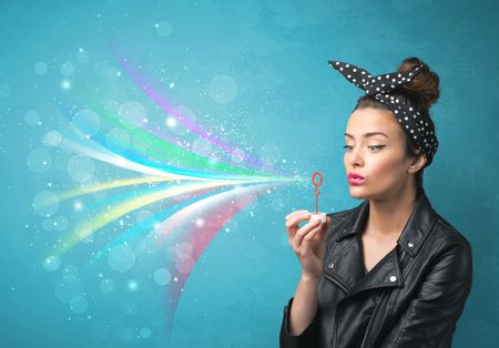 Beautiful girl blowing abstract colorful bubbles and lines on blue background
