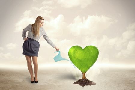 Business woman watering heart shaped green tree concept on background