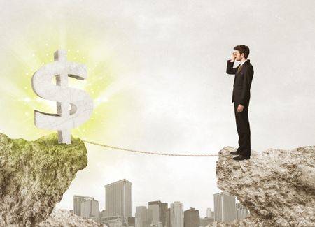 Businessman standing on the edge of mountain with a shining dollar mark on the other side 