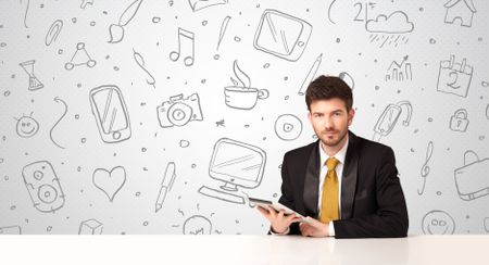 Businessman sitting at table with hand drawn media icons and symbols