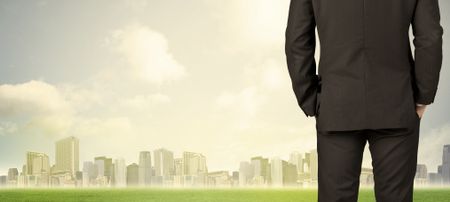 Businessman from the back in front of a city view with clouds and grass