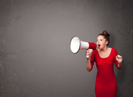 Pretty girl shouting into megaphone on copy space background