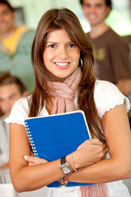 Beautiful female student smiling and holding a notebook in the classroom