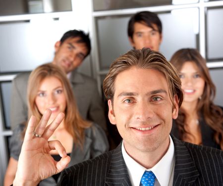 businessman doing the ok sign smiling with his team behind him