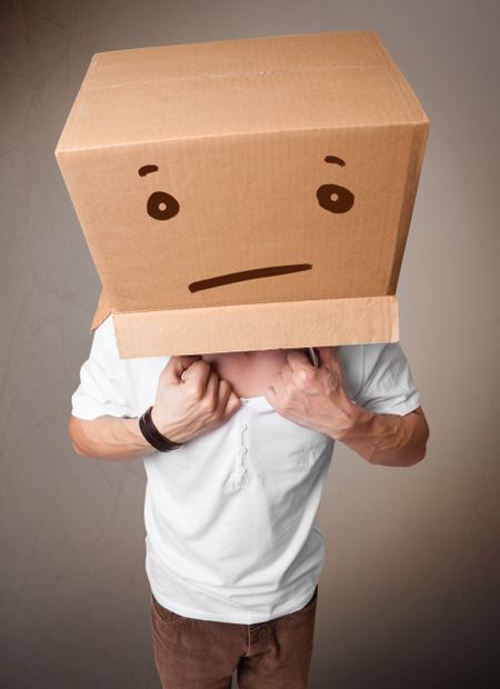 Young man standing and gesturing with a cardboard box on his head with straight face