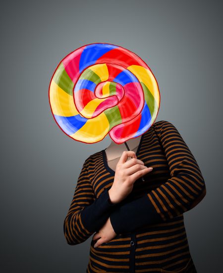 Young lady holding a colorful striped lollipop in front of her head