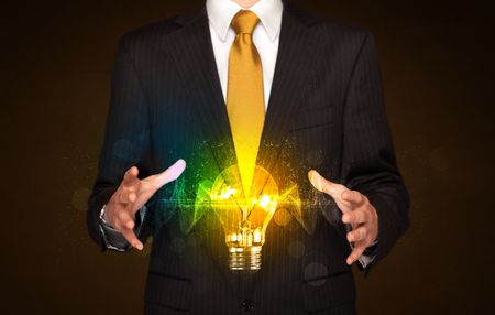 Businessman holding a shining light bulb in front of his body 