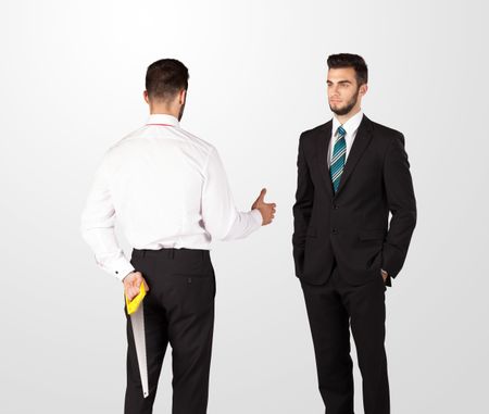 two-opposing-businessman-shake-hands-hiding-245019331 Two opposing businessman shake hands, one of them hiding a weapon behind his back