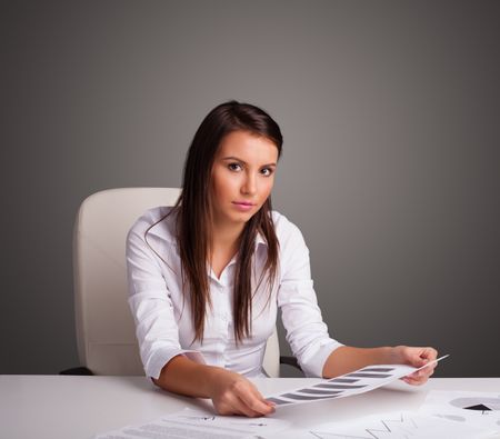 Beautiful young businesswoman sitting at desk and doing paperwork