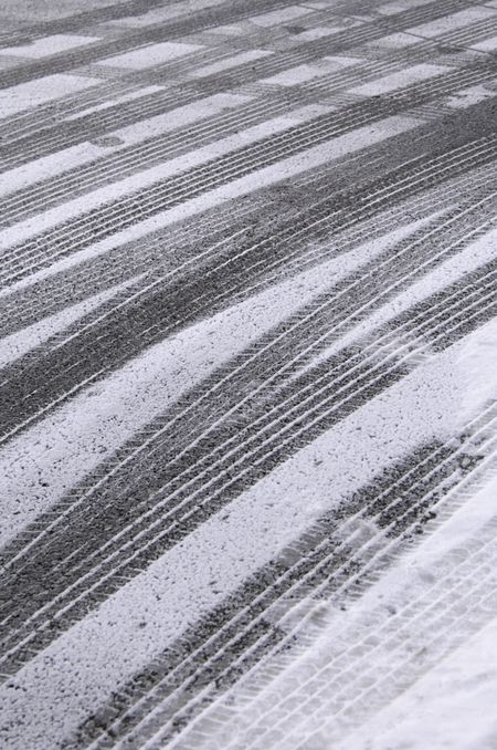 Multiple tracks of car tires, with a few footprints, in snow on pavement