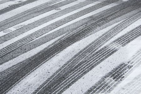 Multiple tracks of car tires, with a few footprints, in snow on pavement