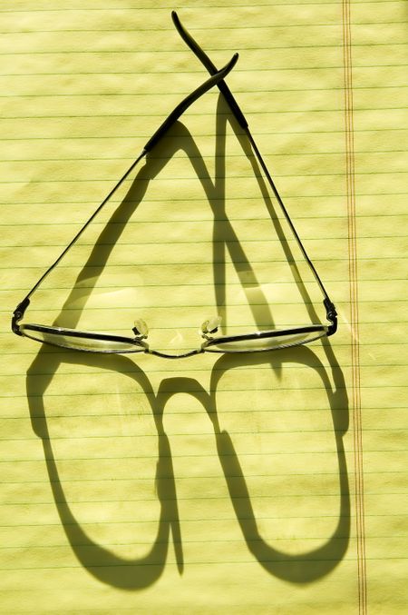 Reading glasses shadowed by sunlight on canary paper