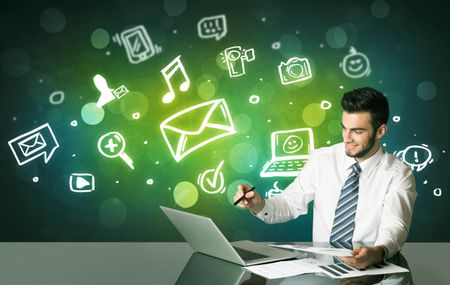 Businessman sitting at the black table with social media symbols on the background