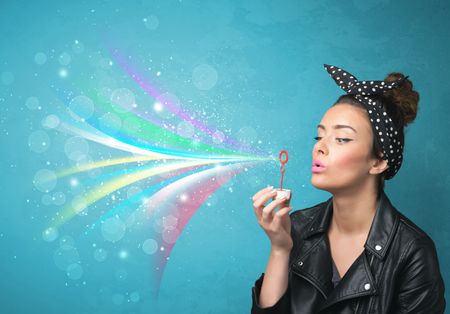 Beautiful girl blowing abstract colorful bubbles and lines on blue background